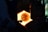 A person is engaged in the process of glassblowing, manipulating a glowing piece of glass inside a furnace. The furnace emits a bright orange light, casting shadows on the surrounding equipment and the person.