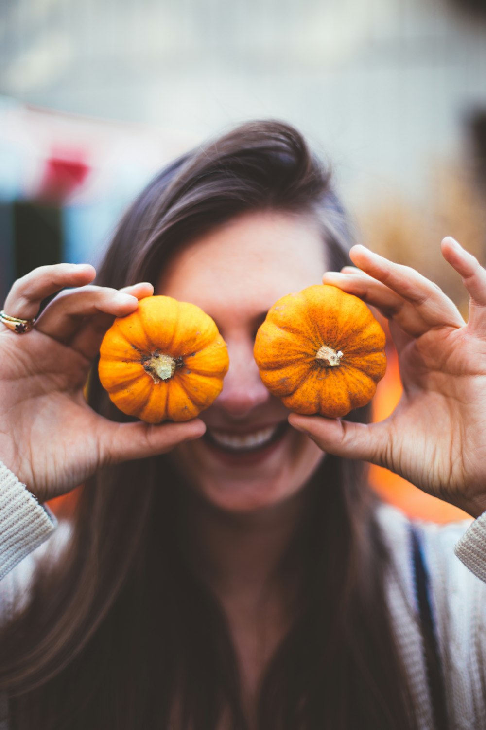 woman holding two orange pumpkins covering her eyes