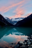 A serene lake in the Rockies at sunset, reflecting the pink and orange sky.