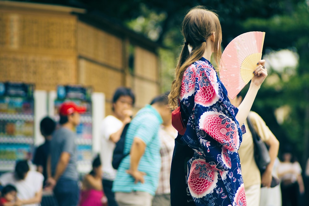selective focus photography of woman holding hand fan beside road
