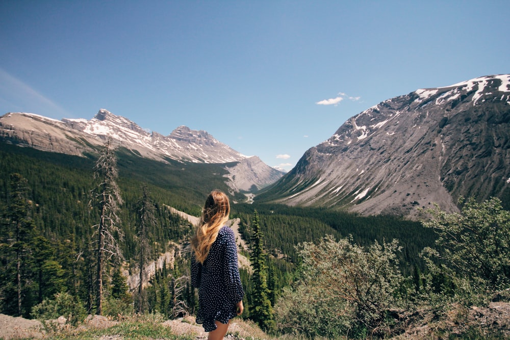 femme debout devant la chaîne de montagnes sous le ciel bleu clair pendant la journée
