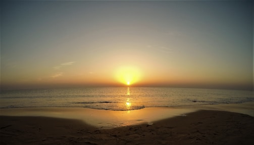 A serene beach scene at sunset with golden sands and calm waves.