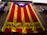 A large banner with red and yellow vertical stripes, featuring a blue triangle with a white star at the top. The text 'assemblea.cat' is visible on the yellow portion of the banner. The banner is draped over a stone building with several balconies.