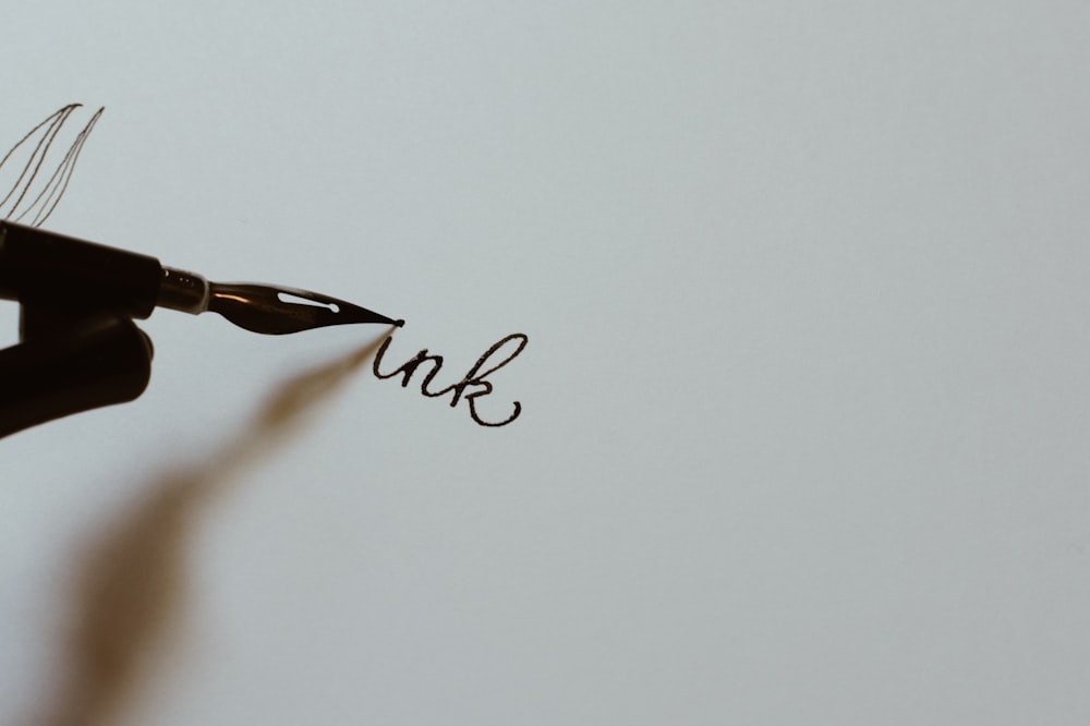 Fotografía de primer plano de la persona que sostiene la pluma estilográfica negra escribiendo texto de tinta en papel blanco