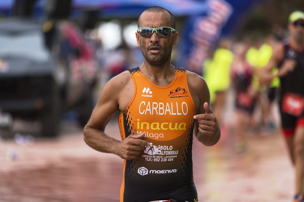 Hombre con camiseta sin mangas naranja y gafas de sol deportivas con montura gris