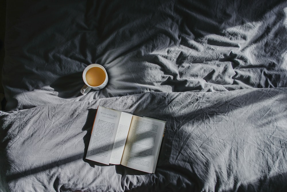 white ceramic mug beside book on gray textile