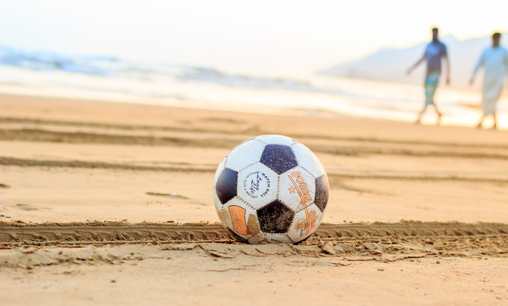 soccer ball on brown sand with two man in the background