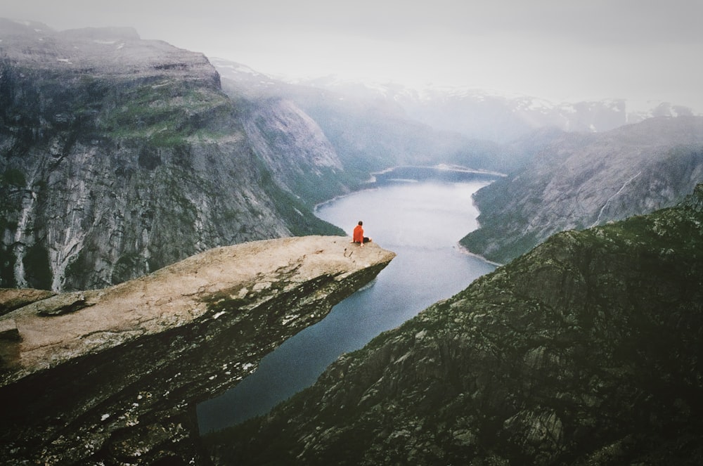 person wearing red shirt sitting on the boulder near the mountain