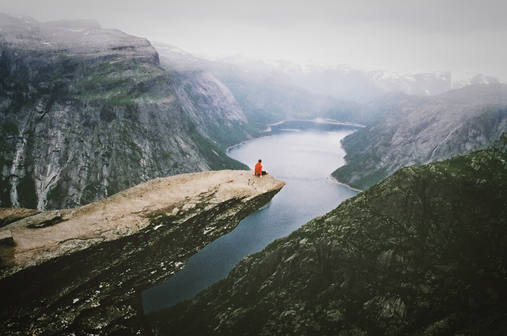 Persona che indossa la camicia rossa che si siede sul masso vicino alla montagna