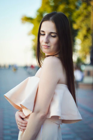 Model wearing a flowing beige dress standing in soft sunlight with a serene expression.