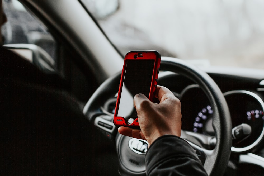 車両のハンドルの前に座っている赤いスマートフォンを持っている人