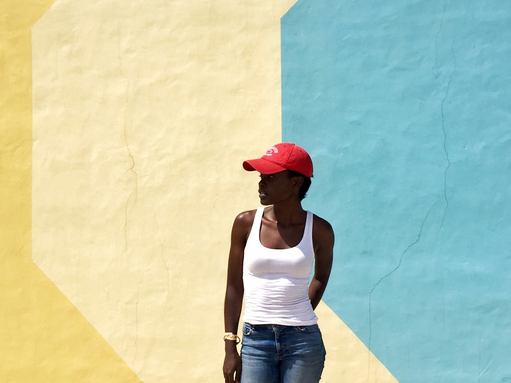 mulher vestindo regata branca em pé ao lado da parede pintada de bege e azul durante o dia