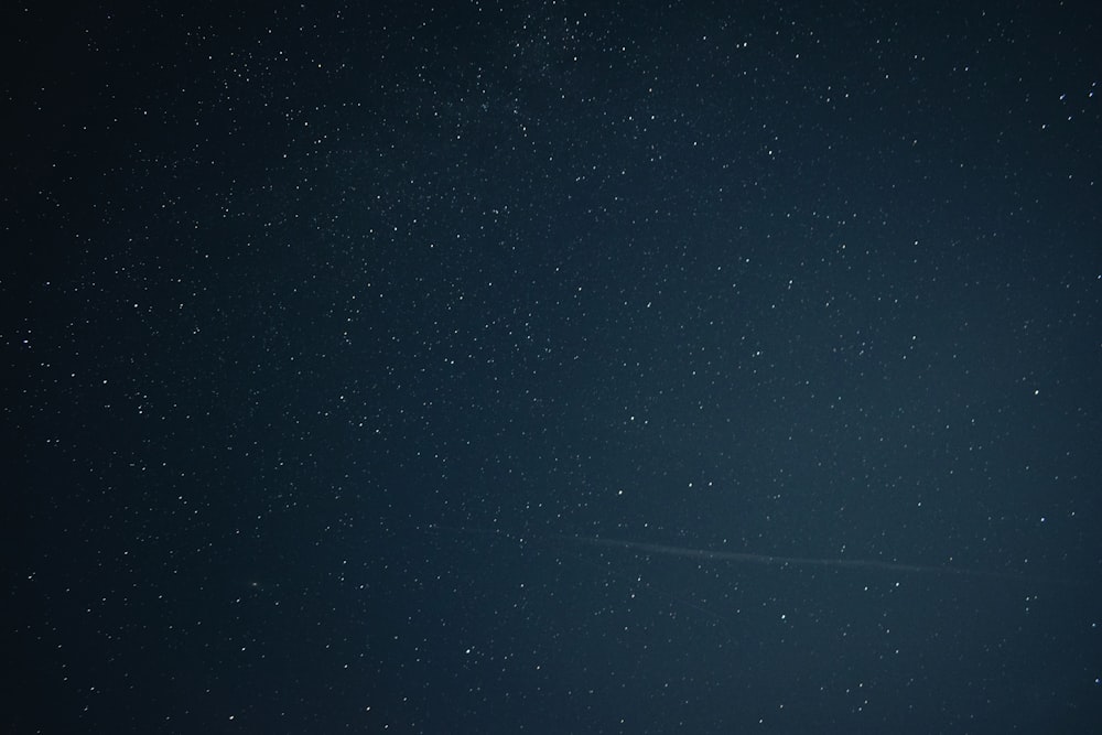 a night sky with stars and a plane in the distance