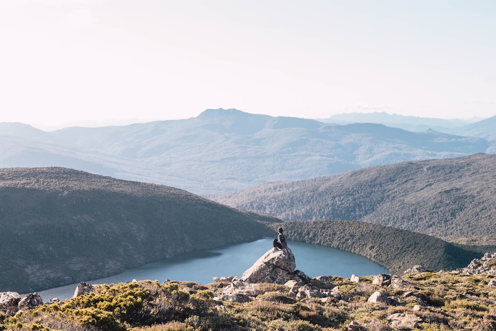 person sitting on brown rock in front of body of water