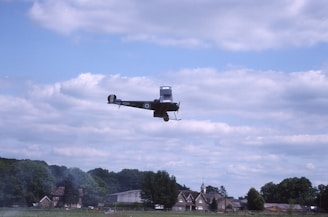 A classic biplane soaring above rolling green hills under a clear blue sky.