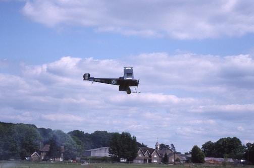 A classic biplane soaring above rolling green hills under a clear blue sky.