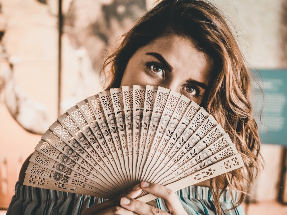 photography of woman holding brown hand fan