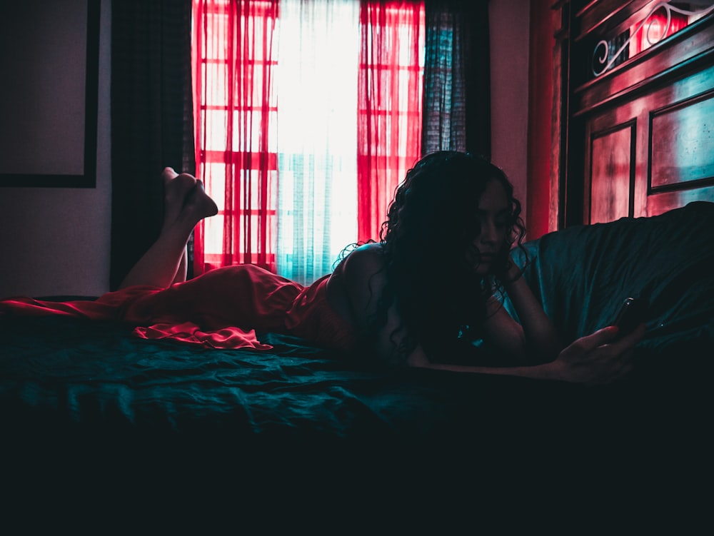 Frau liegt in der Nähe des Bettes, während sie ein Smartphone benutzt
