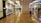 A spacious shopping mall corridor with reflective marble flooring. Storefronts line both sides, displaying mannequins dressed in various outfits. Shoppers are casually walking, adding to the leisurely atmosphere. The lighting is bright and evenly distributed, enhancing the polished look of the interior.