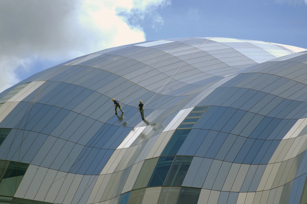 two person standing on glass-panel building under cloudy sky