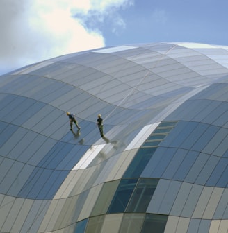 two person standing on glass-panel building under cloudy sky