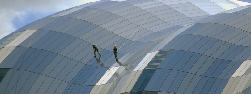 two person standing on glass-panel building under cloudy sky