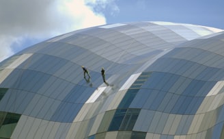 two person standing on glass-panel building under cloudy sky