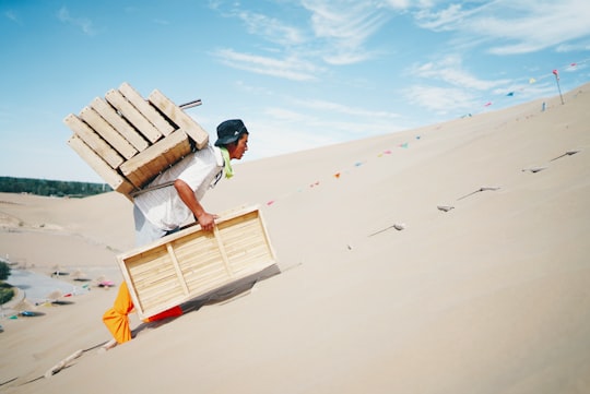 man wearing white shirt carrying brown wooden boxes in Dunhuang China