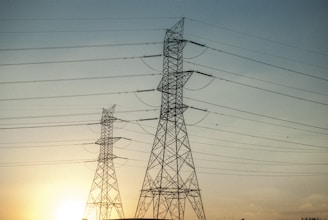 High-voltage transmission towers silhouetted against a clear blue sky at sunrise.