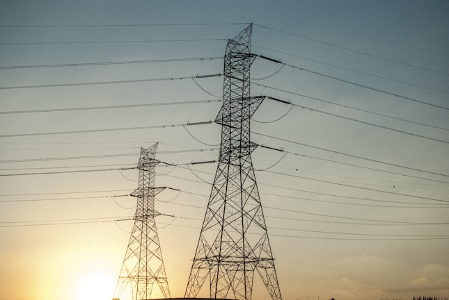 A towering 500 kV transmission line stretching across a clear blue sky at sunrise