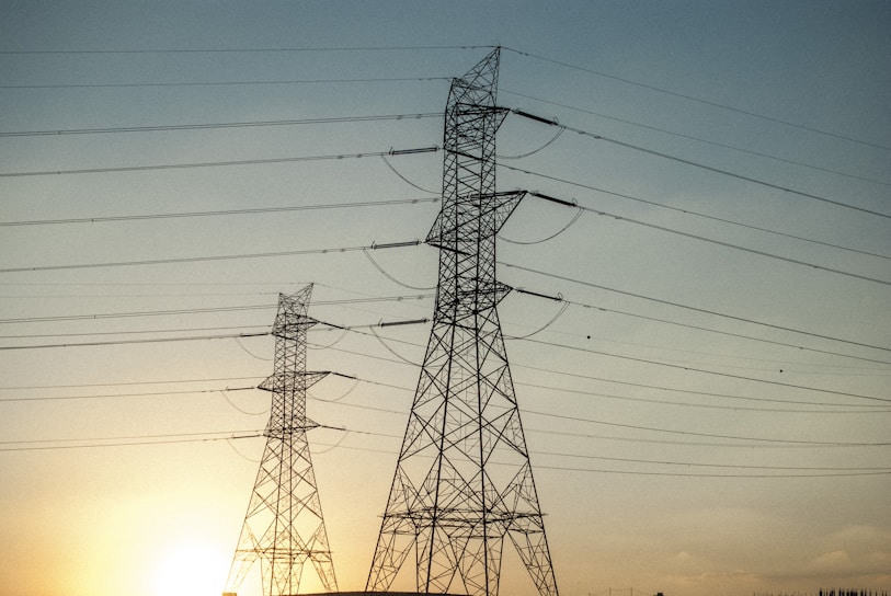High-voltage transmission towers silhouetted against a clear blue sky at sunrise.