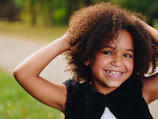 girl wearing black vest raising two hands near green grass field during daytime