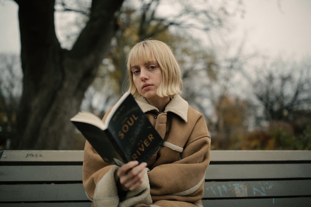 Frau hält Buch in der Hand, während sie auf einer grauen Bank sitzt
