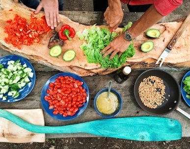 person slicing green vegetable in front of round ceramic plates with assorted sliced vegetables during daytime