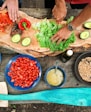 person slicing green vegetable in front of round ceramic plates with assorted sliced vegetables during daytime