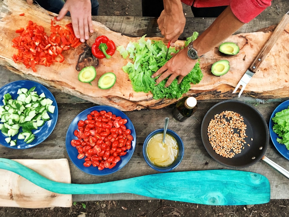 pessoa cortando vegetais verdes na frente de pratos de cerâmica redonda com vegetais fatiados variados durante o dia