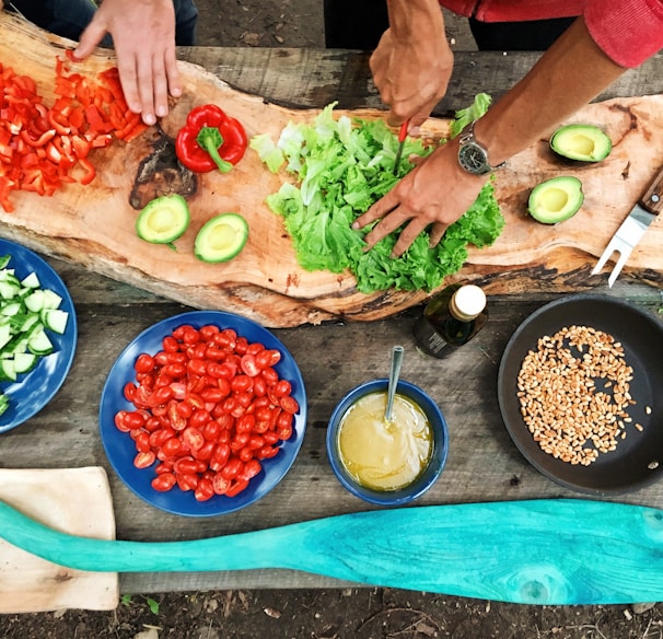 person slicing green vegetable in front of round ceramic plates with assorted sliced vegetables during daytime