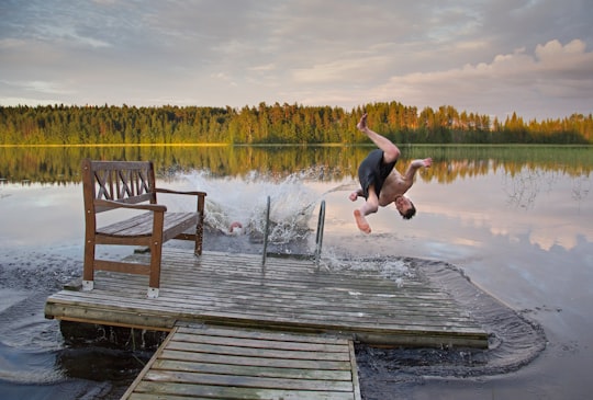 man in black tank top and black shorts jumping on water during daytime in Sulkava Finland