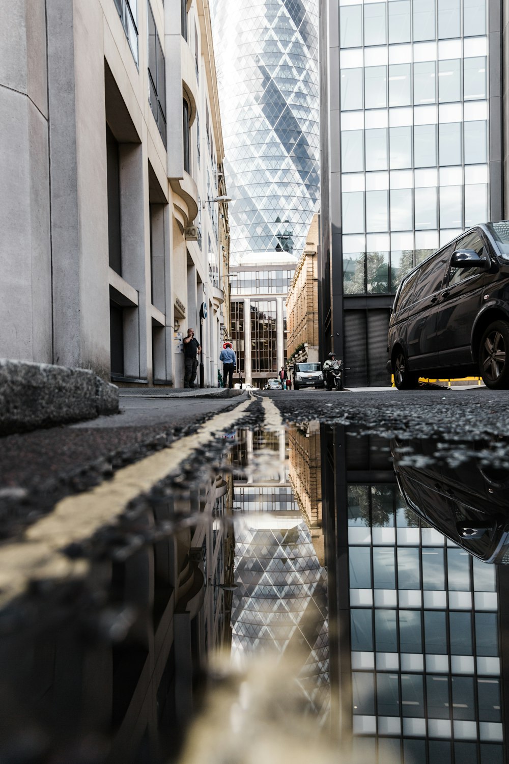 puddle on roadside showing reflection of black vehicle beside highrise buildings