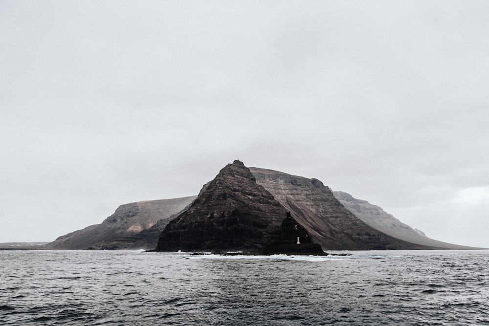 brown mountain beside body of water under grey cloudy sky