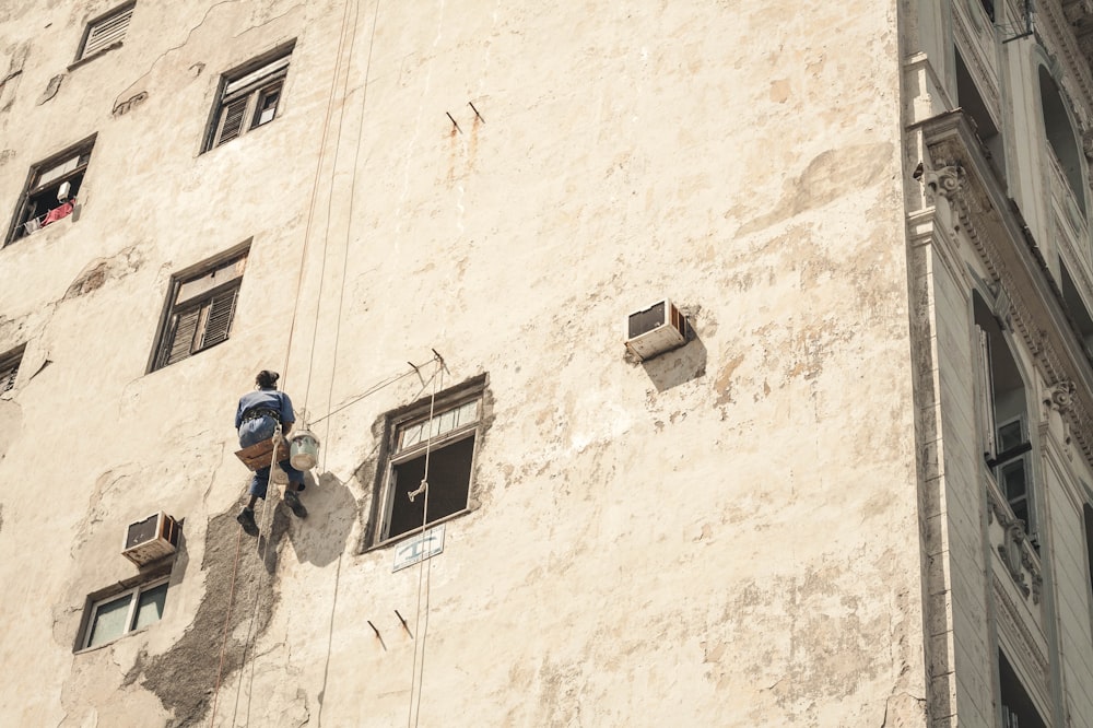 homem pintando edifício de concreto branco durante o dia enquanto pendurado