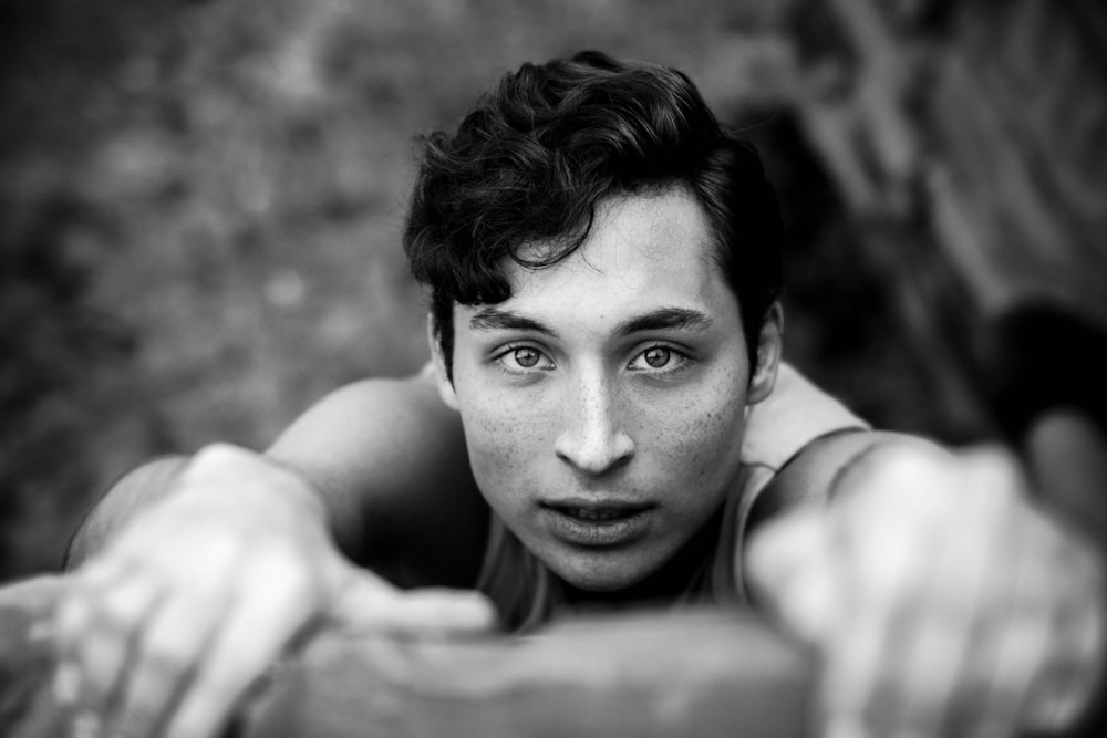 grayscale photography of man hanging on cliff