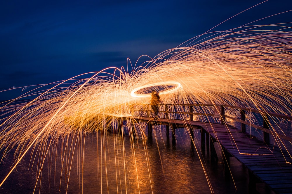 steel wool photography of person standing on sea dock