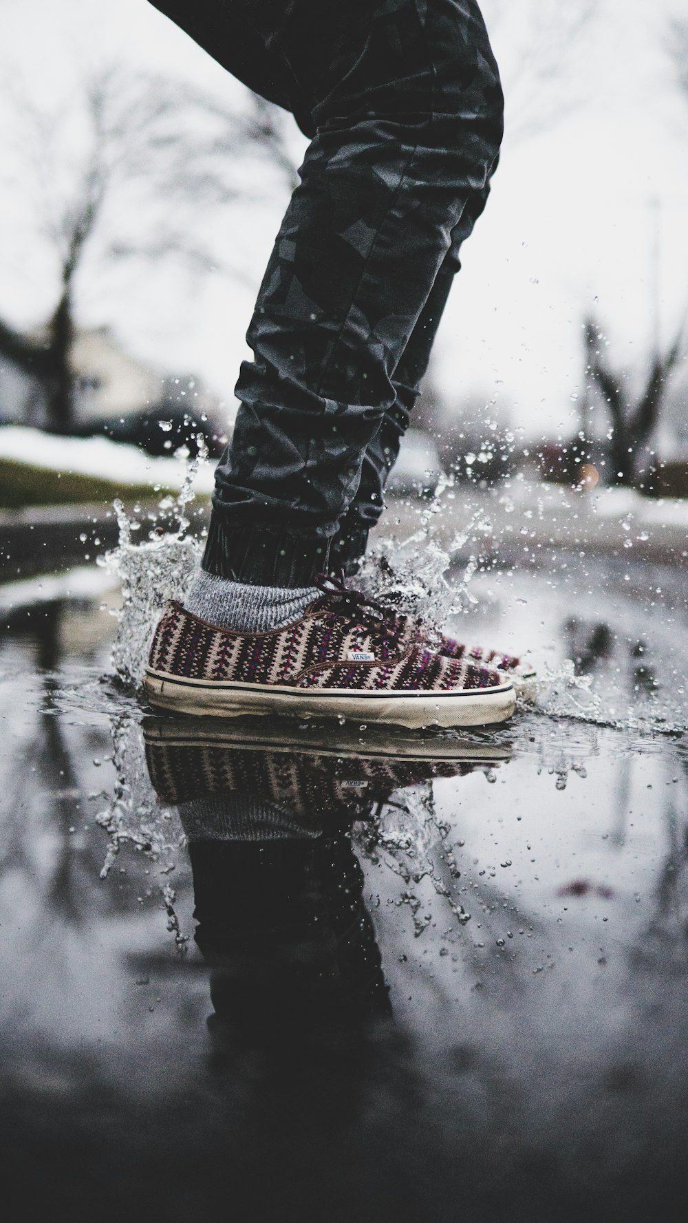 personne portant un pantalon noir et des espadrilles basses noires et blanches sur un sol mouillé