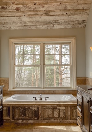 comfort room with white bathtub and brown wooden cabinets