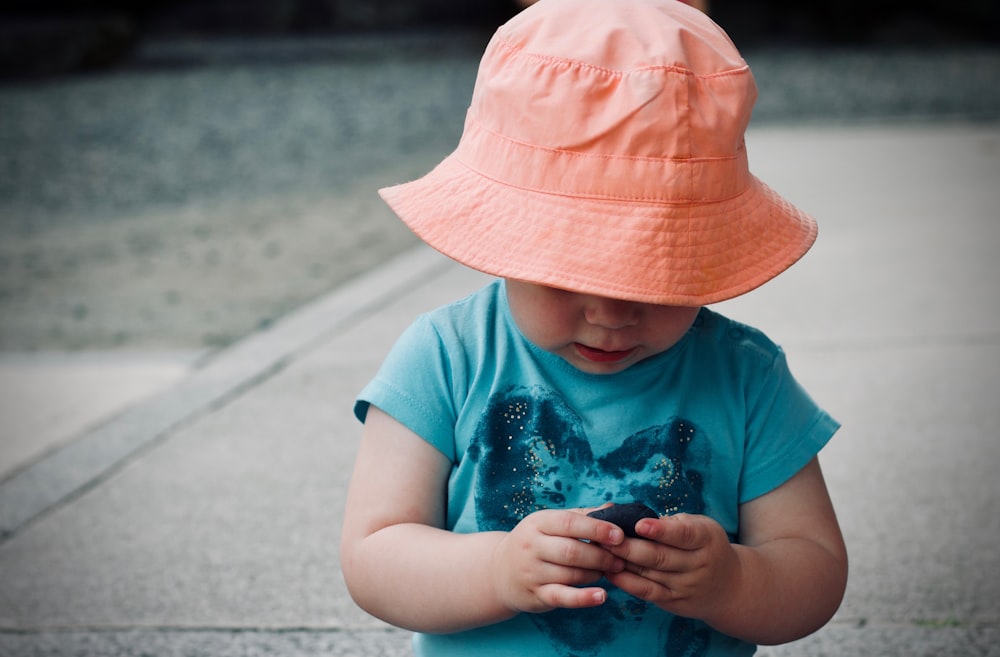 baby wearing blue shirt and orange bucket hat