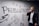 A person dressed in business attire is talking on a mobile phone while standing next to a wall decorated with motivational drawings and the word 'Productivity' in bold letters. The wall features symbols like hearts, arrows, and checklists.