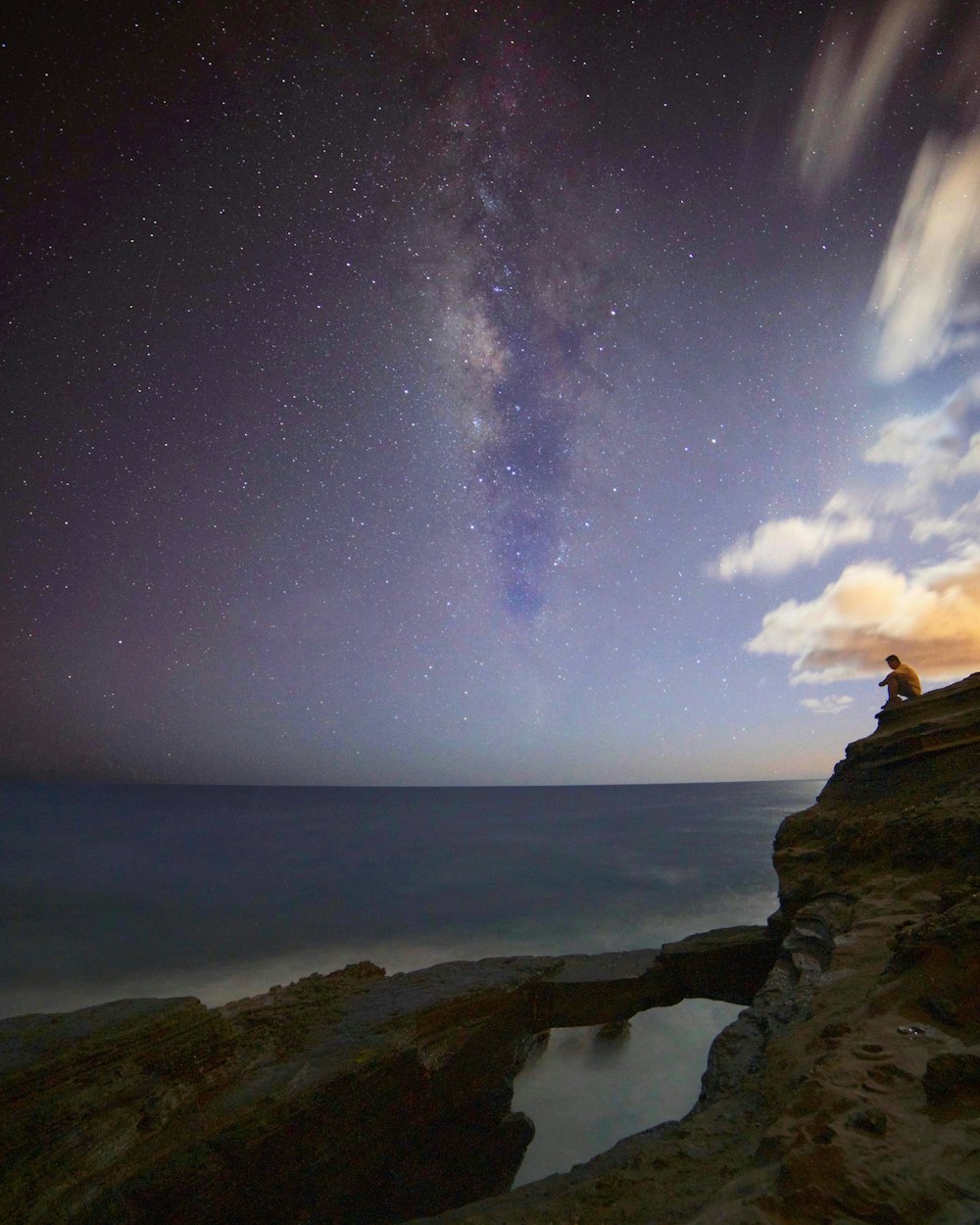 a person sitting on a cliff looking at the stars