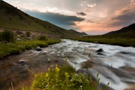 A peaceful river flowing through a lush green valley at sunset.