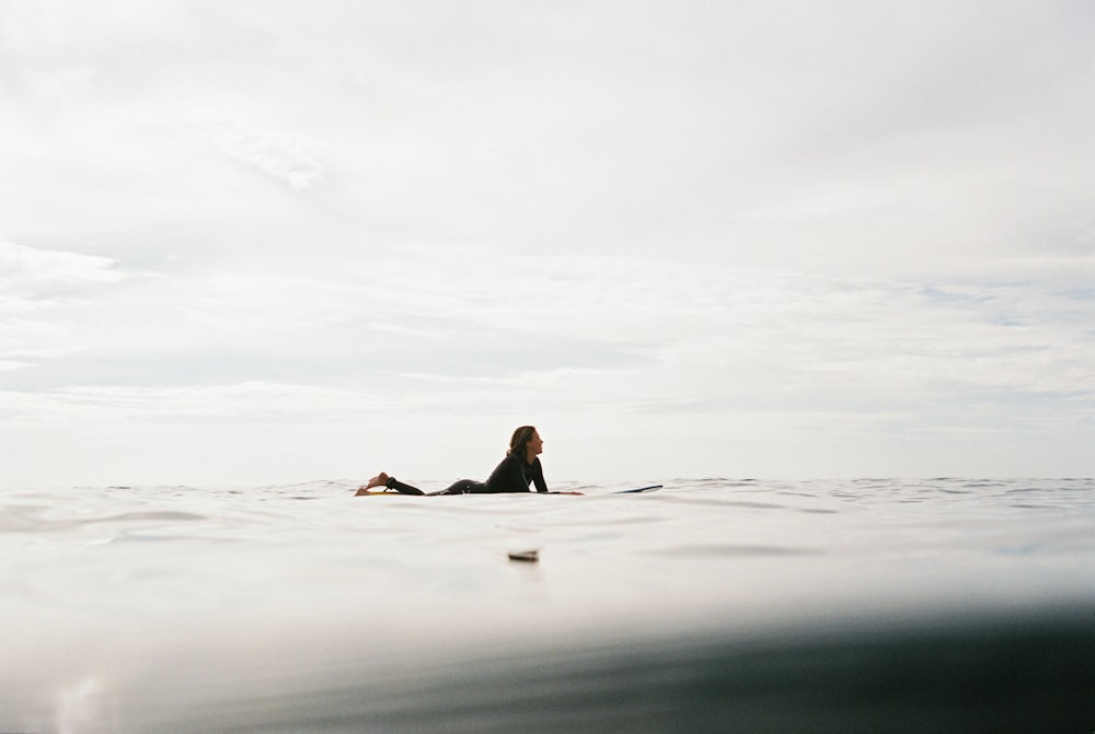 woman lying on surfboard on body of water